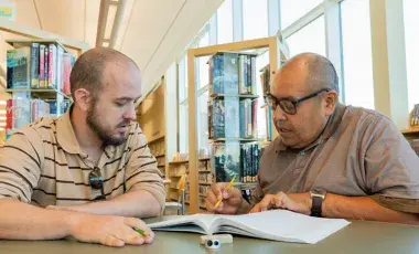 two people sitting at a table. One person is tutoring the other