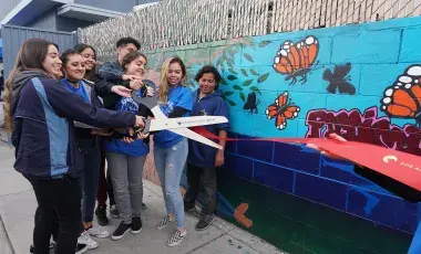 teens with giant scissors cutting a ribbon by a painted mural