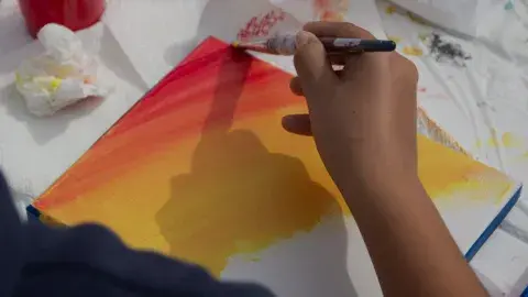 a person's hand is painting a sunset on canvas