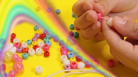 rainbow and colorful beads and children's hands putting beads on string 