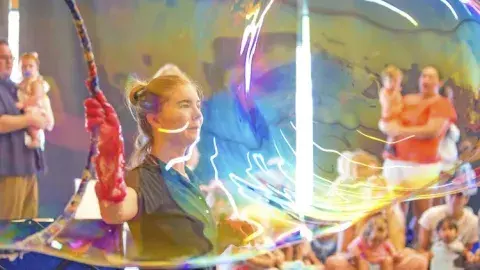 Instructor making a big bubble with a big hoop while families watch.