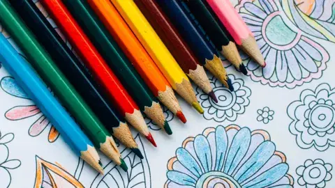 Photo is of different colored pencils on top of a colored in page with designs.