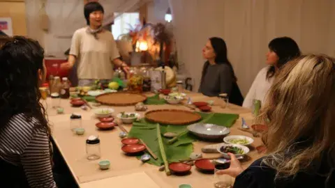 Chef Jess Wang teaching a cooking class to a table full of patrons. 
