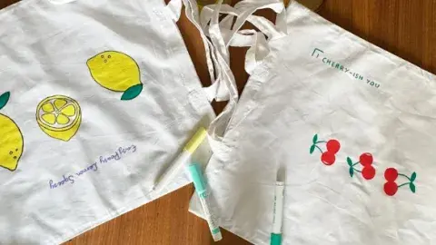 White canvas tote bags decorated with colorful fruit drawings and fabric markers on a table.